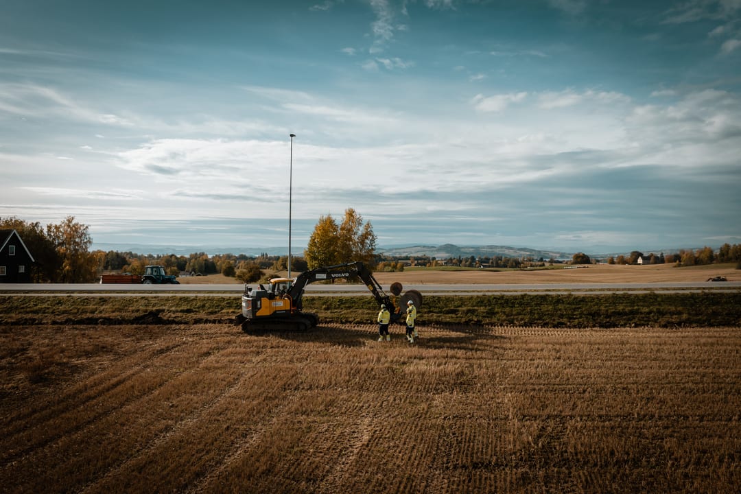 Two people and an excavator working in a large field next to a road.