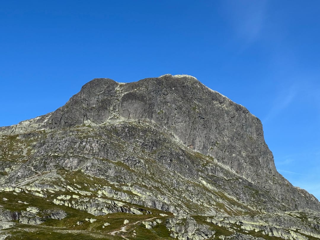 Massiv fjellvegg med grønne fjellhyller og klar blå himmel, fotografert på en solrik dag i høyfjellet.